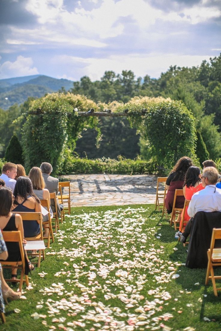 an outdoor ceremony with white flowers on the grass and people sitting in wooden chairs watching