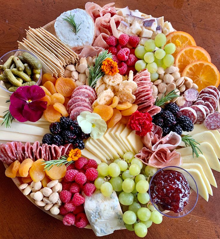 a platter filled with cheese, meats, fruits and vegetables on a wooden table