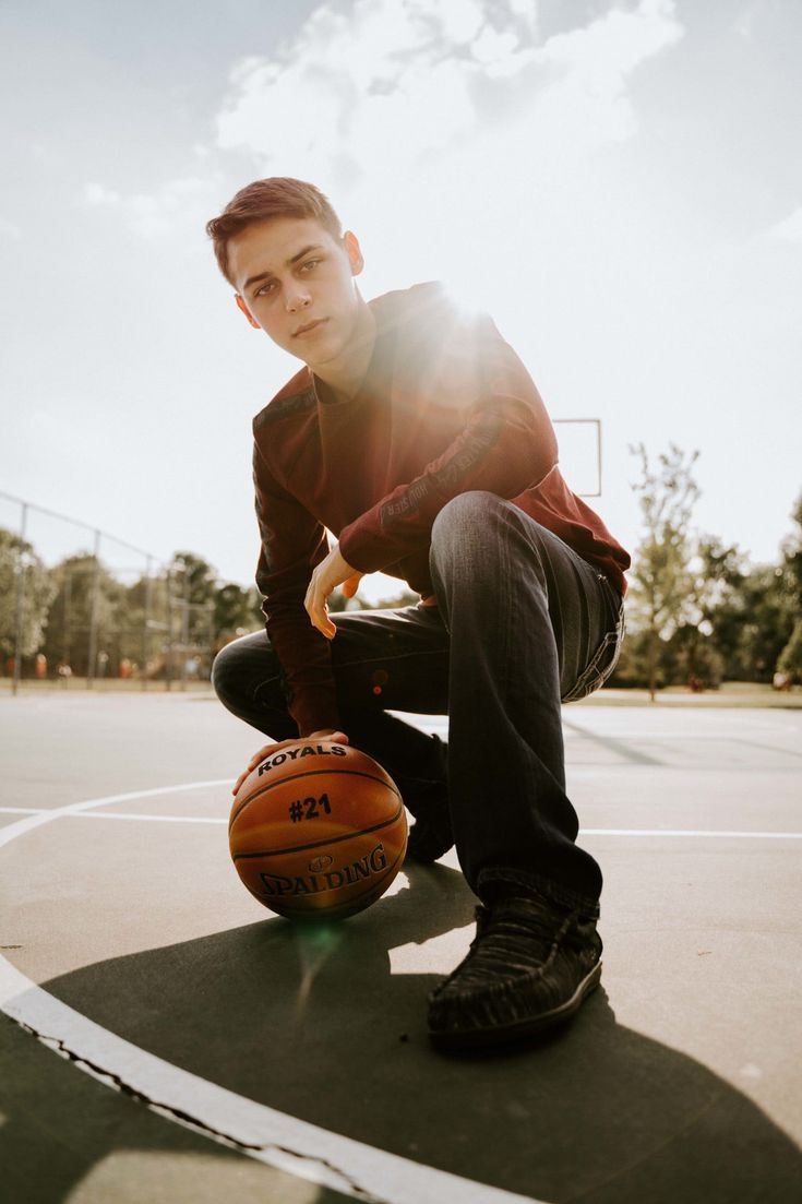 a young man sitting on top of a basketball court holding a basketball in his hand