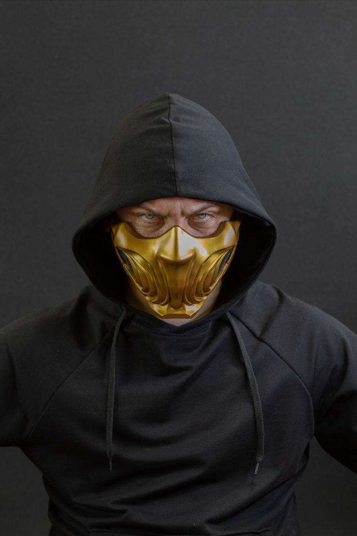 a man in a black hoodie with a gold mask on his face and hands