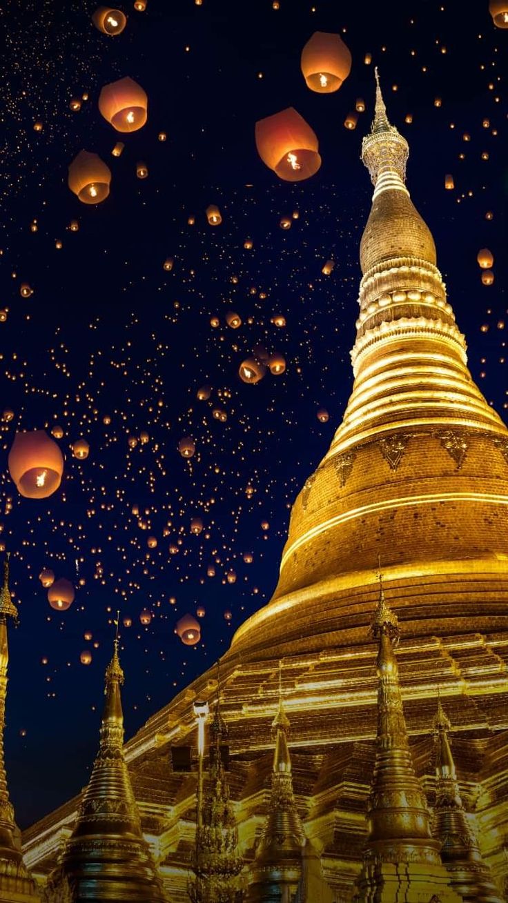 the sky is filled with lanterns floating in the air above a large golden pagoda at night