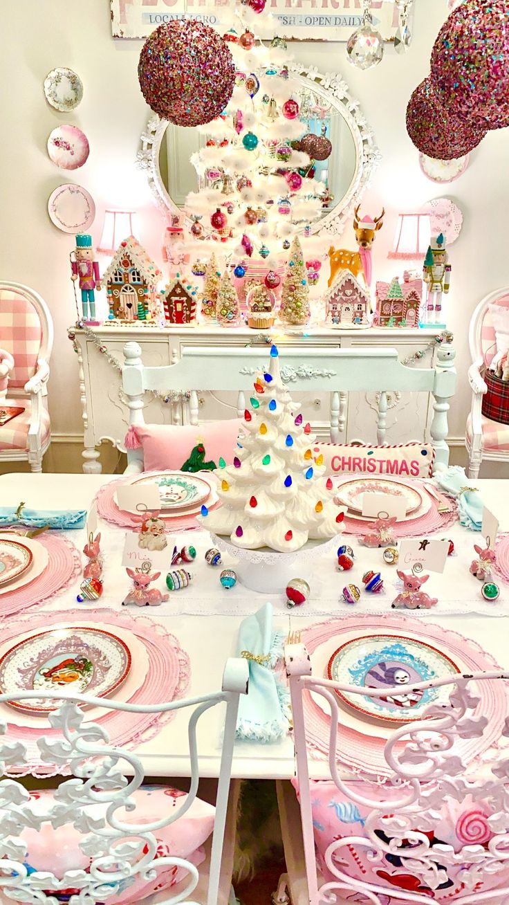 the table is set for christmas dinner with pink and white plates, silverware, and decorations