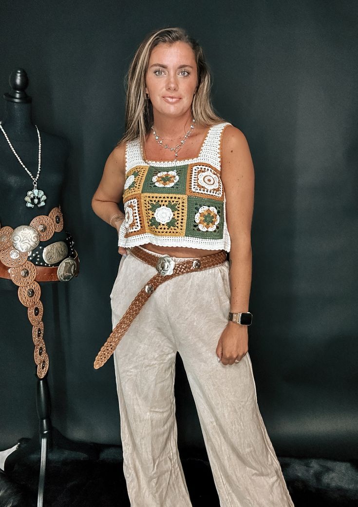 a woman standing in front of a mannequin wearing white pants and a crochet top