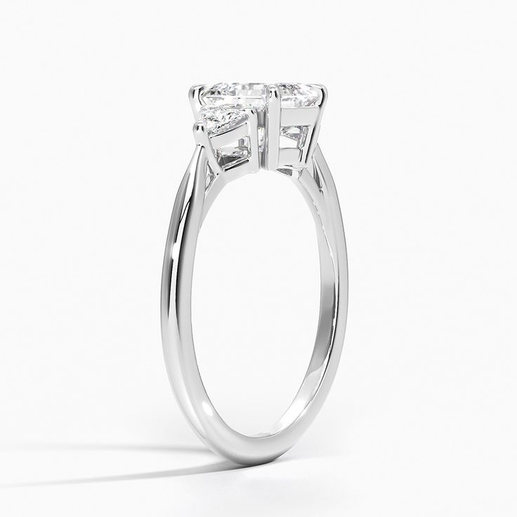 Asscher Cut Trillion Cut Three Stone Classic Diamond Engagement Ring - Platinum. Captivating trillion shaped diamonds brilliantly frame the center gem in this classic three stone engagement ring. The petite band gently tapers and secures the gems within elegant claw prongs (1/8 total carat weight). Modern Heart Cut Wedding Rings, Classic Three Stone Cluster Ring For Formal Occasions, Trillion Cut Three Stone Diamond Ring For Anniversary, Moissanite Three Stone Rings For Anniversary, Anniversary Three Stone Moissanite Rings, Formal Three Stone Cubic Zirconia Wedding Ring, Modern Three Stone Anniversary Rings, Elegant Three Stone Moissanite Wedding Ring, Elegant Three Stone Cluster Ring For Formal Occasions