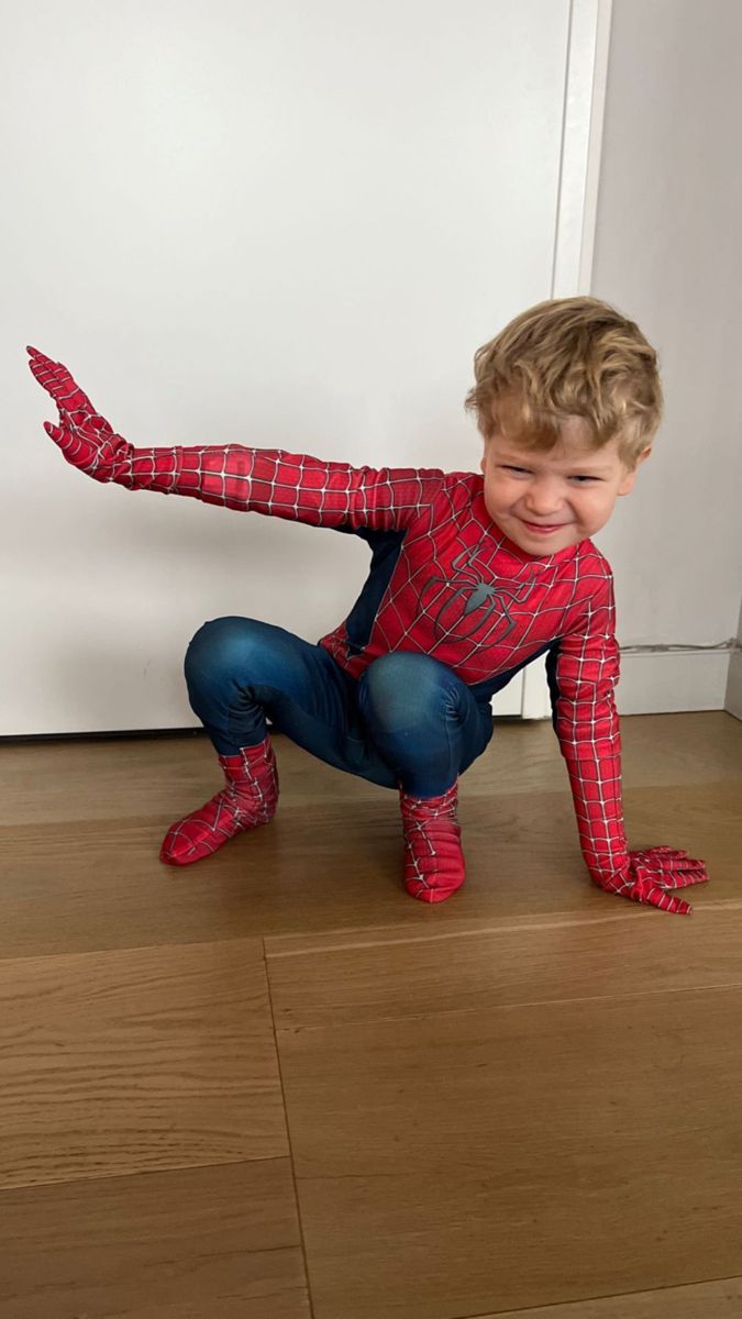 a young boy in a spiderman costume is smiling and stretching his arms out on the floor