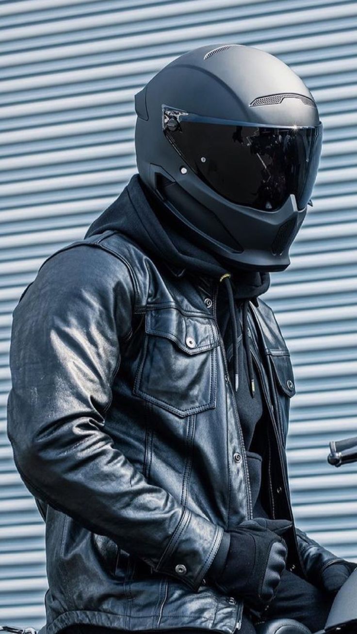 a man wearing a leather jacket and helmet sitting on a motorcycle