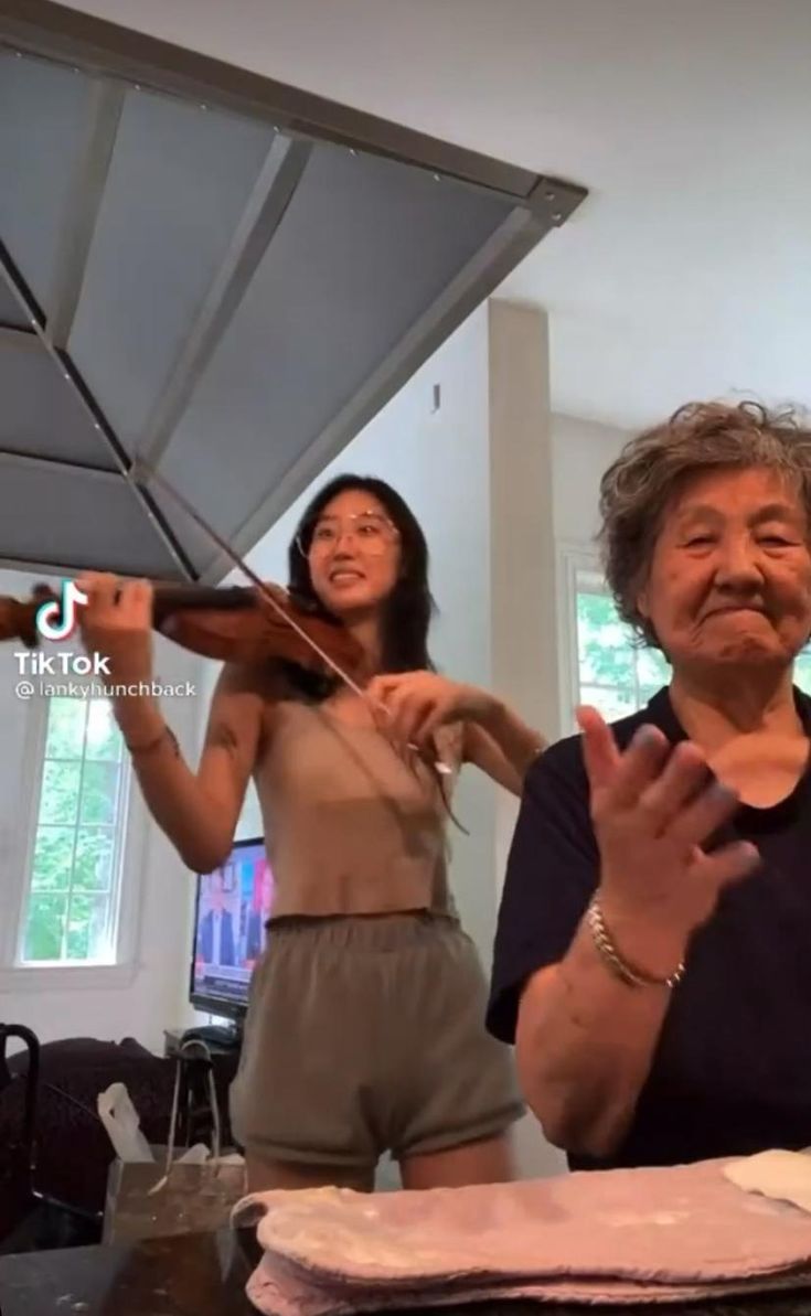 an older woman playing the violin while another woman looks on with her hands behind her back