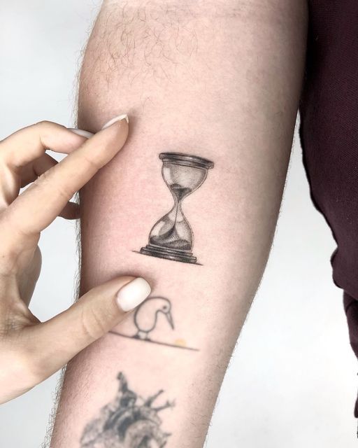 a person with a tattoo on their arm holding an hourglass in front of them