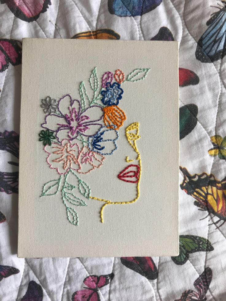 an embroidered portrait of a woman's face with flowers and butterflies around her head