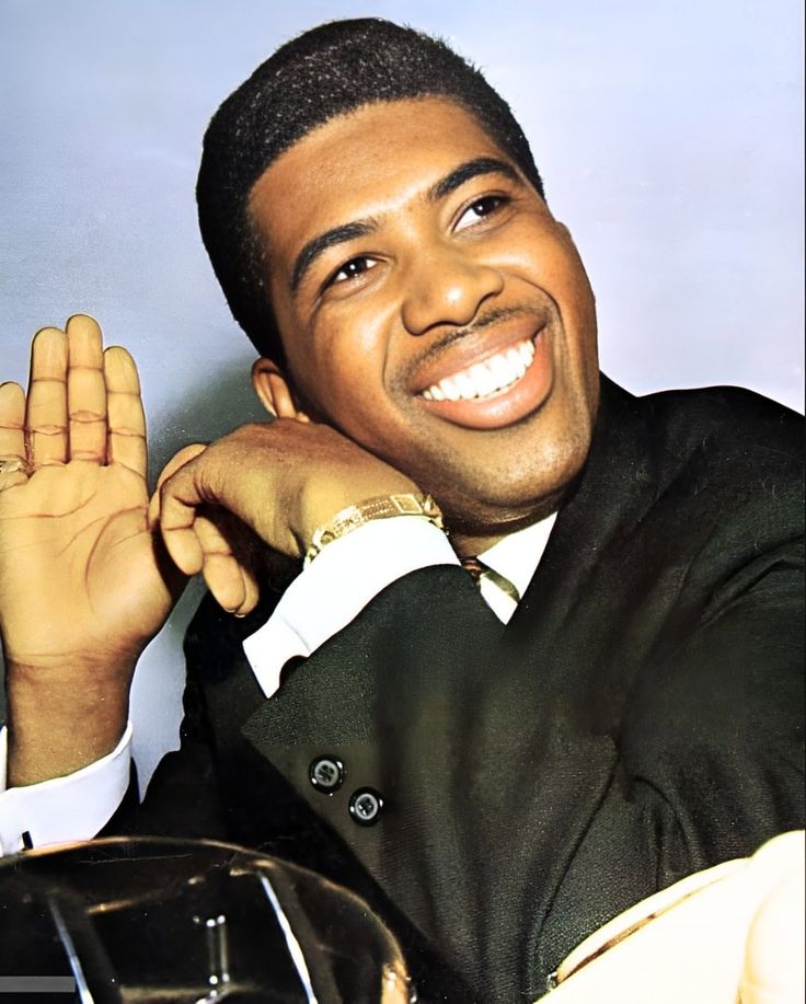 a man in a suit and tie sitting down with his hand up to the side