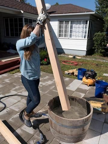 a woman working on a wooden cross in front of a house with tools around her