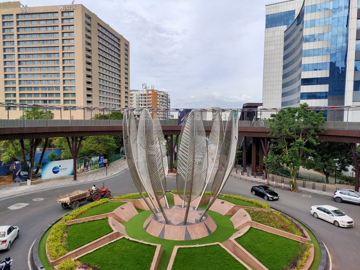 a circular garden in the middle of a road with cars driving on it and tall buildings in the background