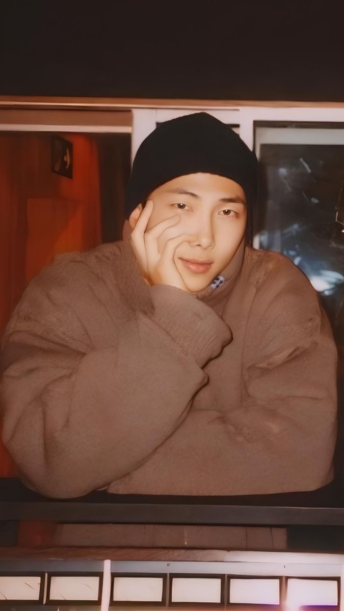 a man in a brown sweater and black beanie is looking at the camera with his hand on his face