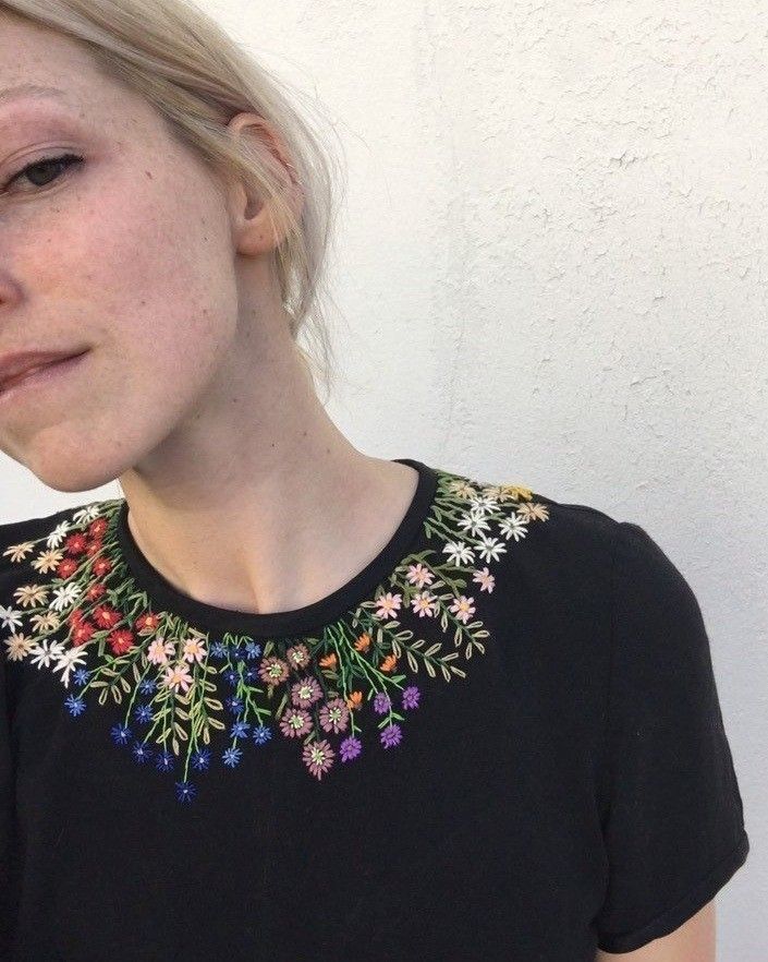 a woman with blonde hair wearing a black shirt and flowered collar necklace on her neck