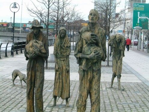 three statues of people standing next to each other on a brick sidewalk in front of buildings