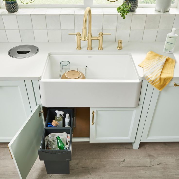 a kitchen sink with an open drawer underneath it and various cleaning supplies in the bottom compartment