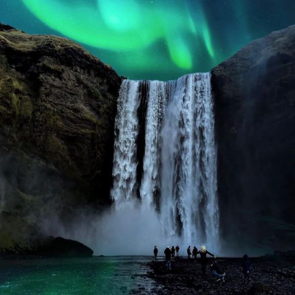 people standing in front of a waterfall under the northern lights