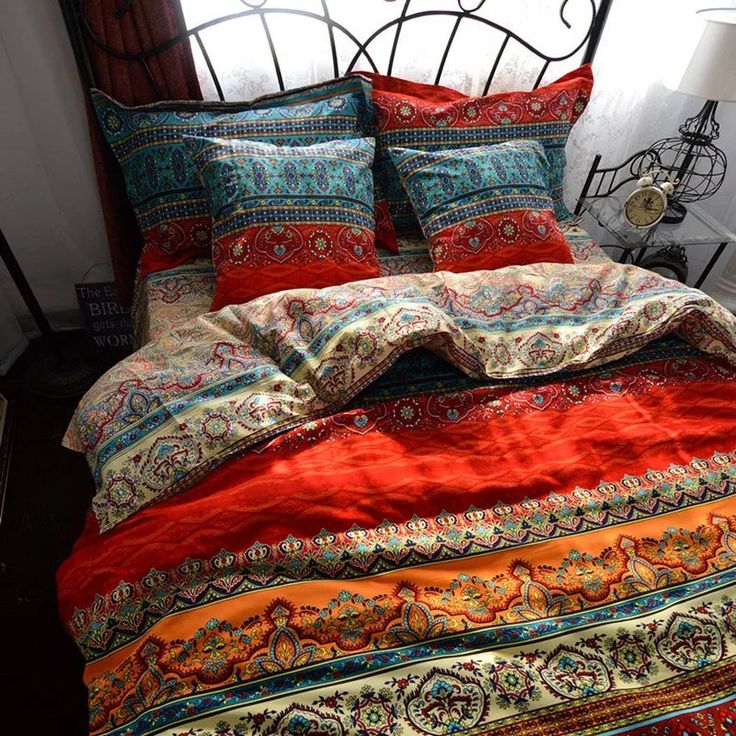 a bed with red and blue comforters on top of it in a room next to a window