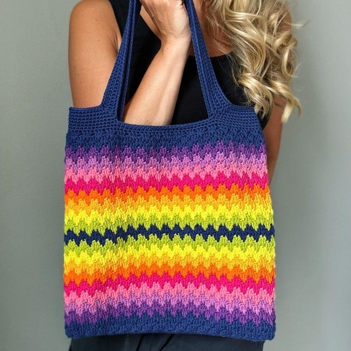 a woman holding a multicolored knitted tote bag in front of her face