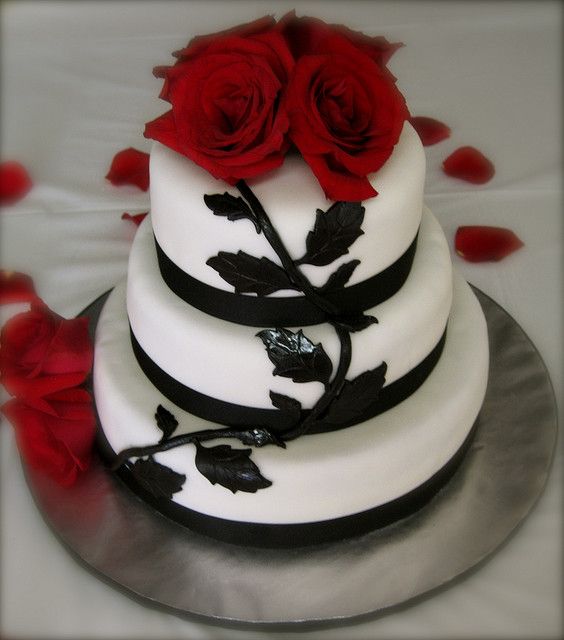 a three tiered wedding cake with red roses on the top and black ribbon around it