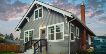 a gray house with white trim and windows on the front porch is shown at sunset