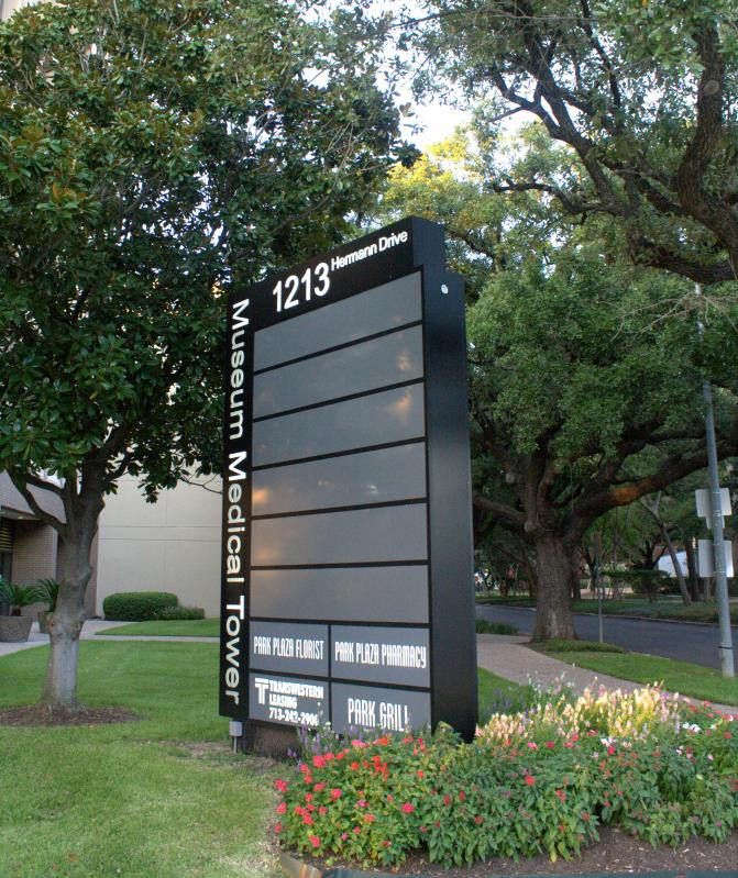 a large sign in front of a building with trees and flowers around it on the grass