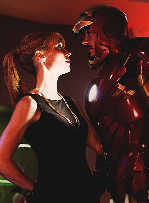 a woman standing next to a man in front of a giant iron man bust up