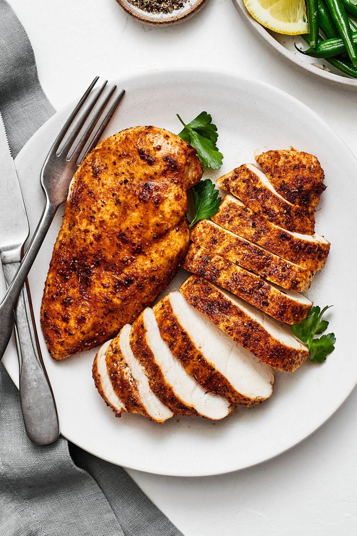 a white plate topped with sliced chicken next to green beans