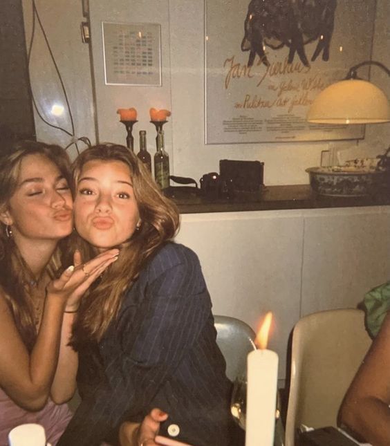 two women sitting at a table with candles in front of them and one woman holding her face