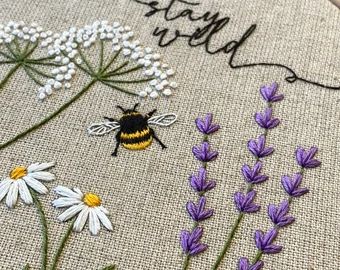 a close up of a cross stitch pattern with flowers and a bee