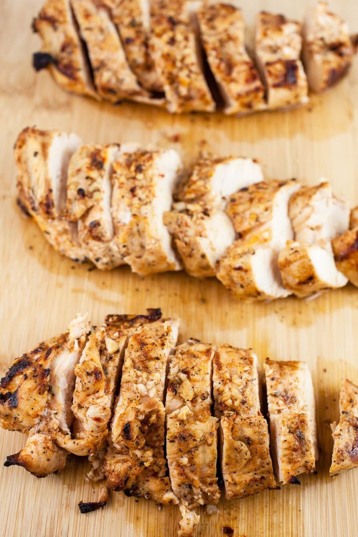 sliced chicken on a wooden cutting board next to another piece of meat with white sauce