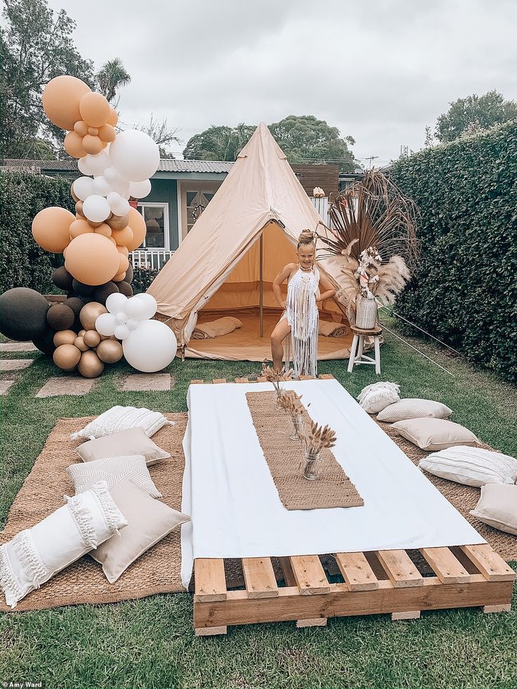 a tent set up with balloons and pillows on the ground in front of some trees