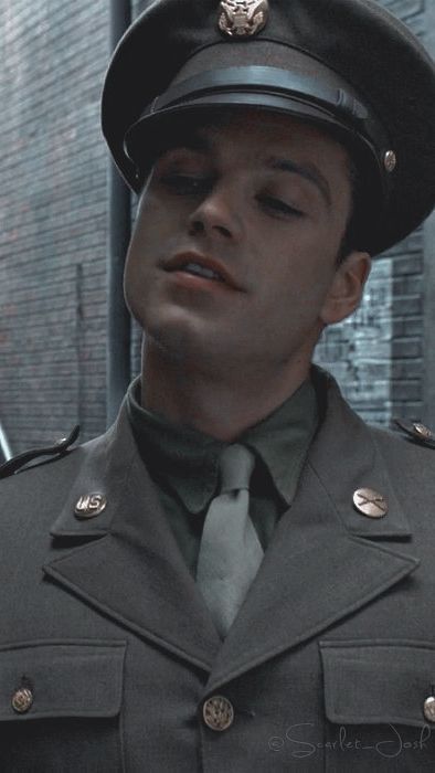 a man in uniform standing next to a brick wall with his eyes closed and one hand on his chin