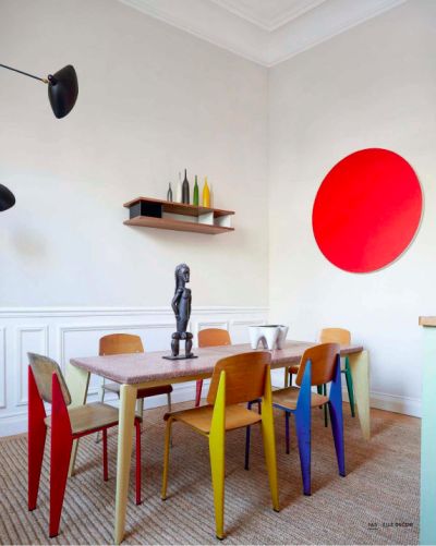 a dining room with colorful chairs and a table in front of a red circle on the wall