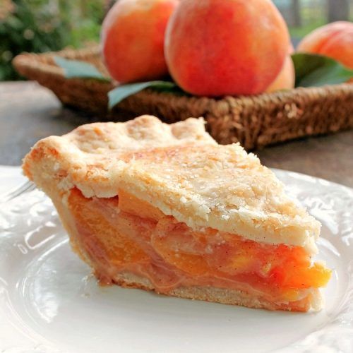 a piece of pie sitting on top of a white plate next to some peaches