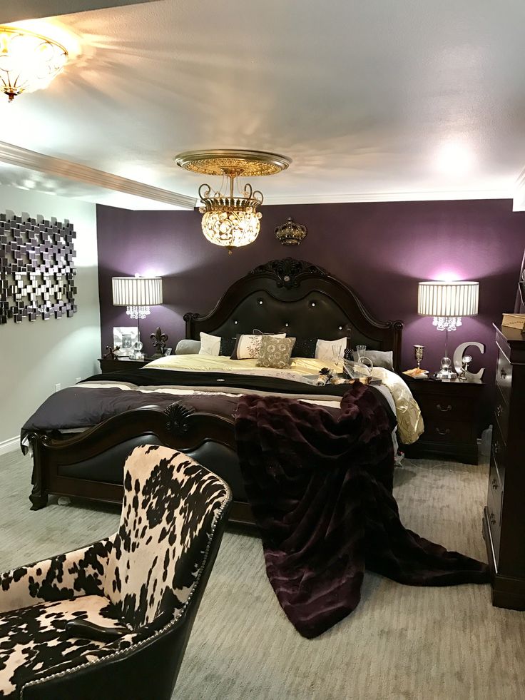 a bed room with a neatly made bed and two chairs next to it in front of a chandelier