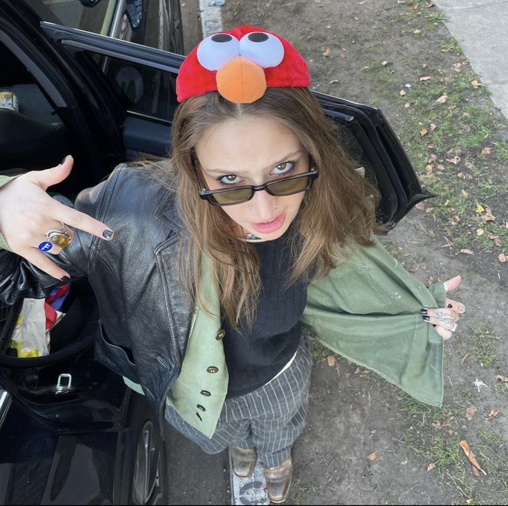 a woman with sunglasses and a red bird on her head standing next to a car