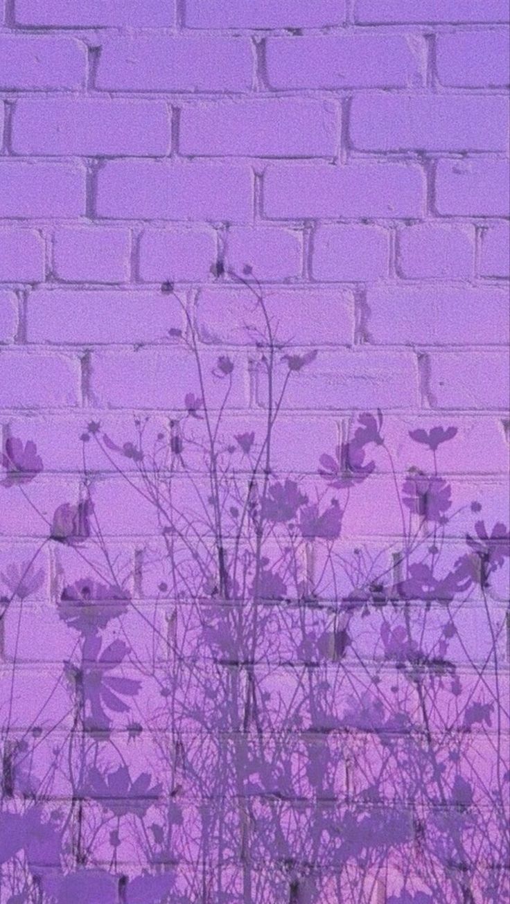 a purple brick wall with trees and bushes in the foreground against a pink sky