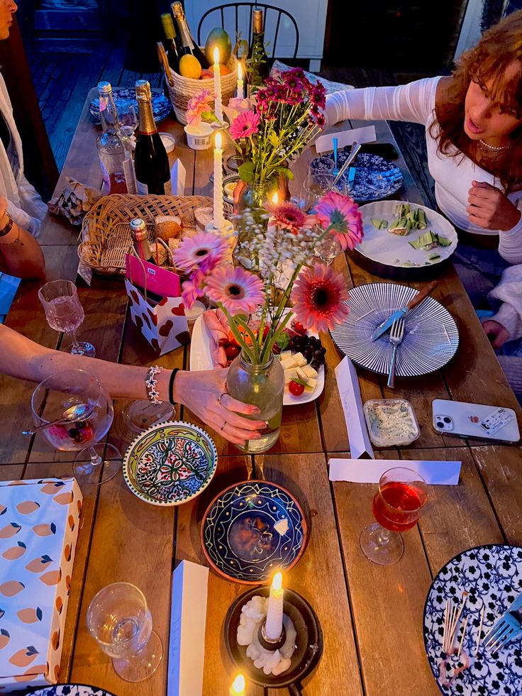 a group of people sitting around a wooden table with plates and candles on it,