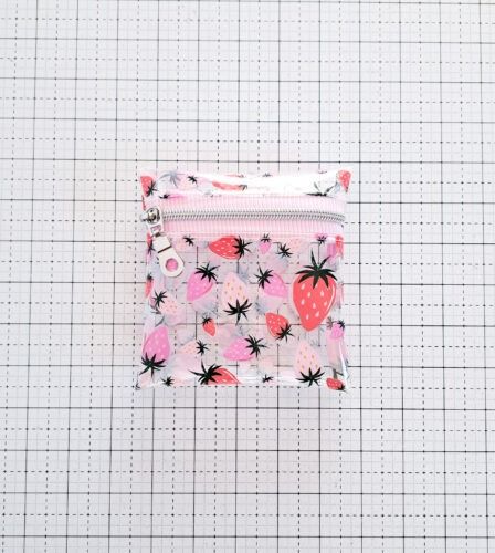 a small zipper bag with strawberries and stars printed on the front, sitting on a gridded surface