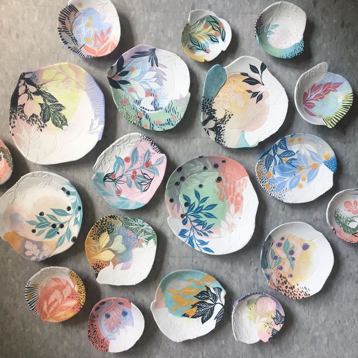 a bunch of plates sitting on top of a table with flowers painted on them in different colors