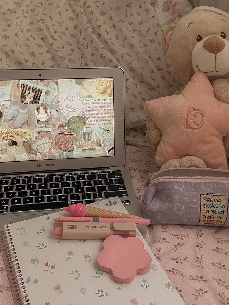 a teddy bear sitting next to a laptop computer on a bed with pink and white sheets