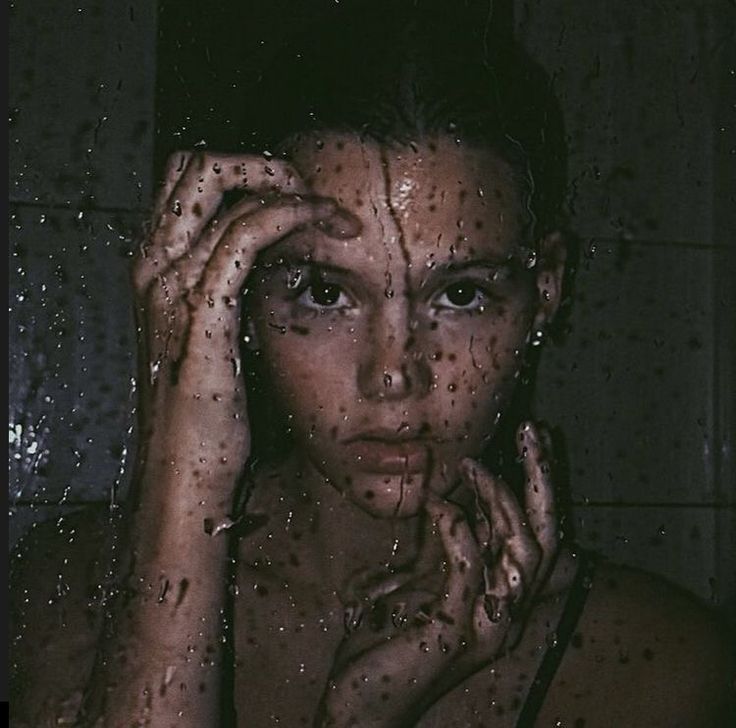 a woman with her hands on her face in the shower, looking at the camera