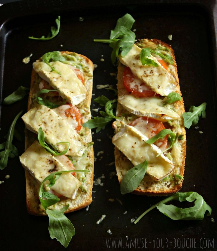 two pieces of bread with cheese and vegetables on it sitting on a black tray next to green leaves