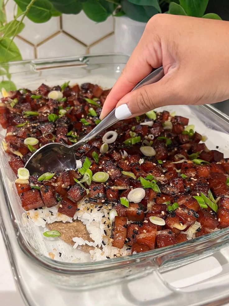 someone using a spoon to scoop food out of a casserole dish with rice and vegetables