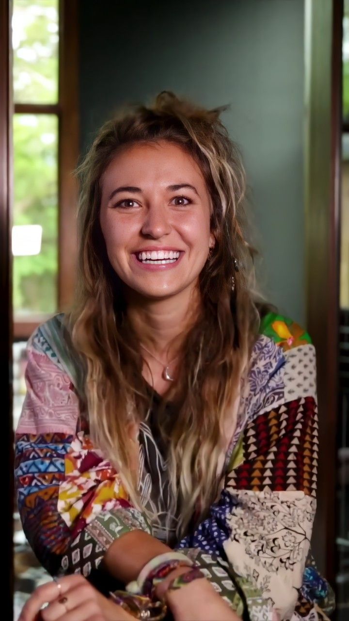 a woman with long hair sitting in front of a window and smiling at the camera