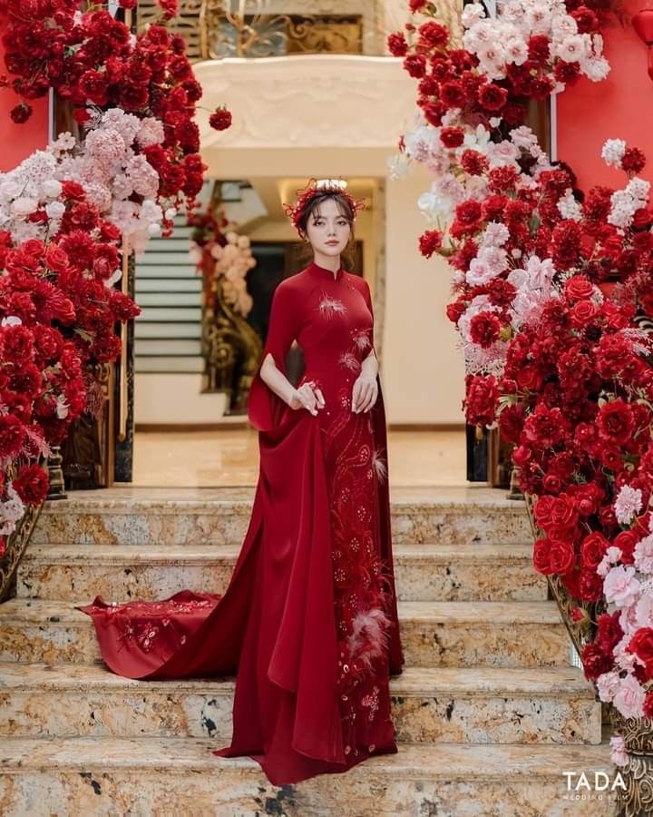 a woman in a red dress standing on some steps with flowers and roses around her