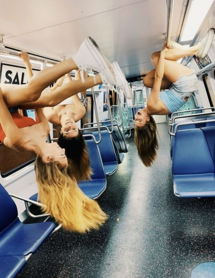 two women upside down on seats in a train or subway car, one with long hair and the other without