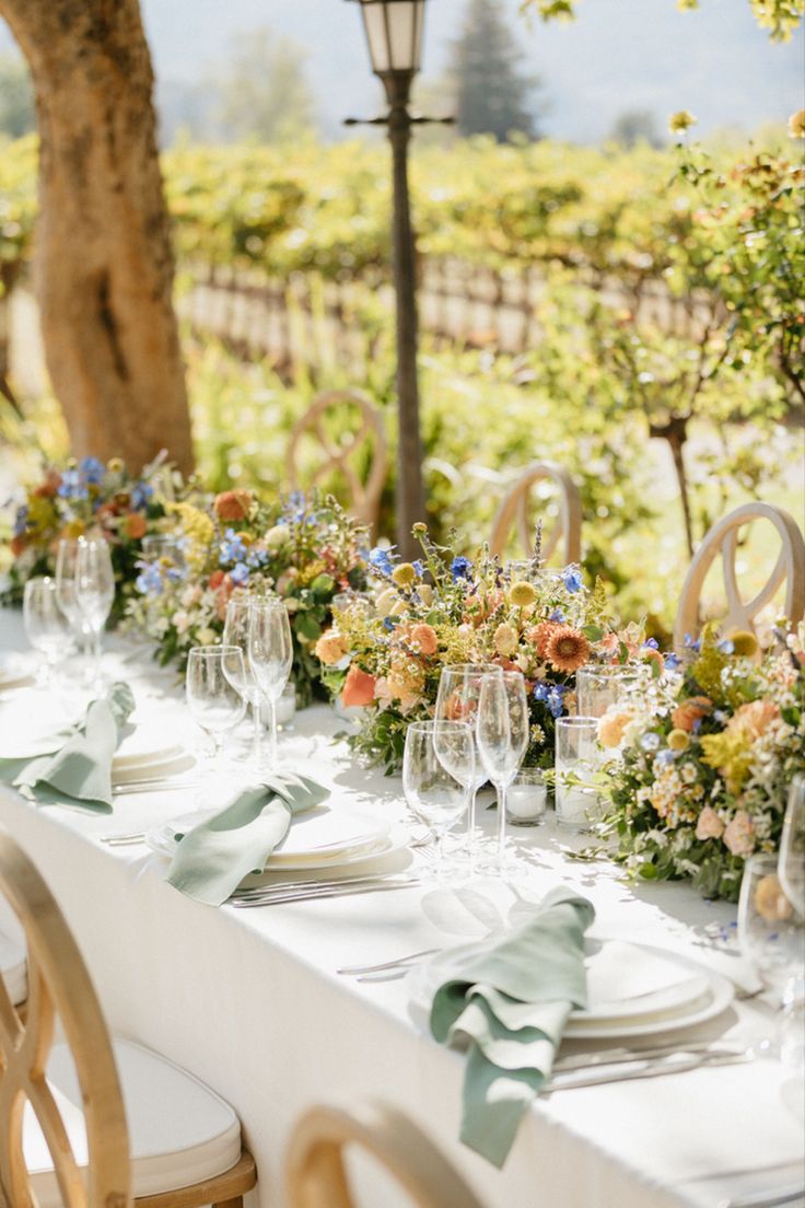 a long table set with place settings and flowers on it for an outdoor dinner party