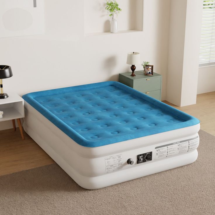 an inflatable mattress is sitting on the floor next to a table and lamp